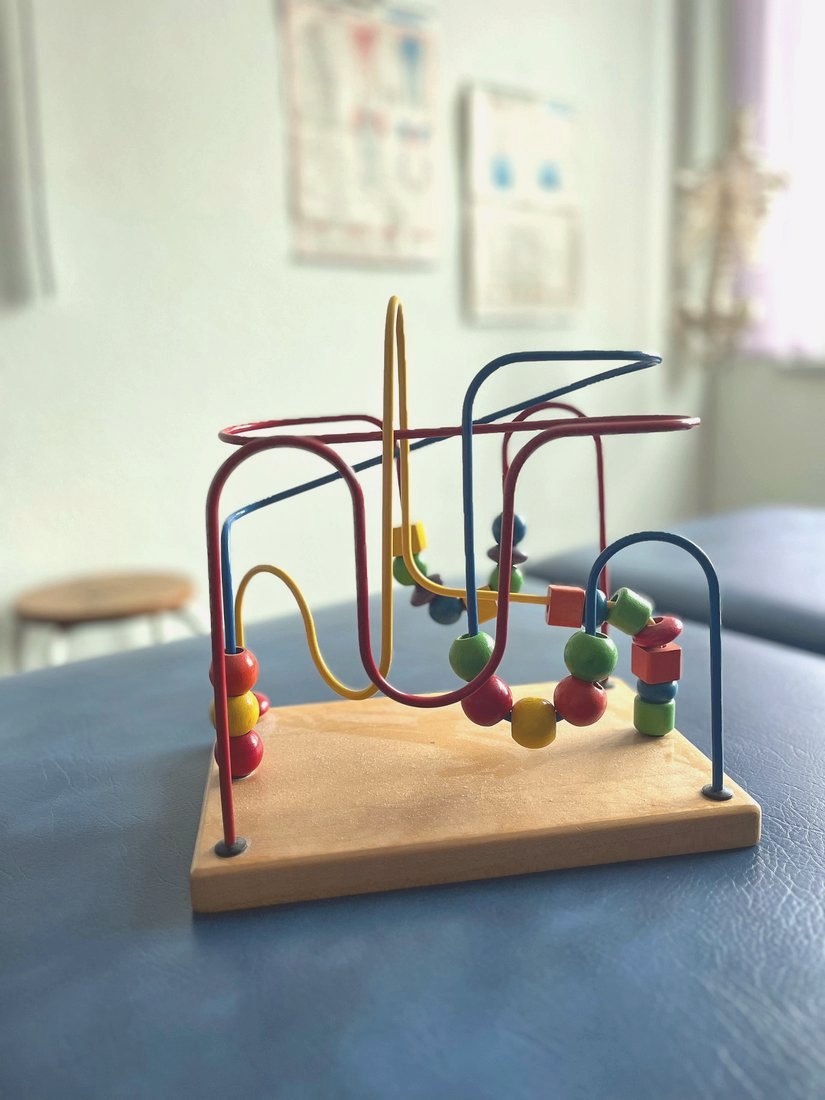 Buntes Holz-Perlenspiel auf einer Behandlungsliege im Therapiezentrum Schrader